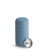 A Fellow Carter Move Mug in blue with a silver strainer lid leaning against it.